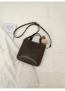 Detail der dunkelbraunen Eimertasche mit einem niedlichen roten Pilz-Plüschanhänger