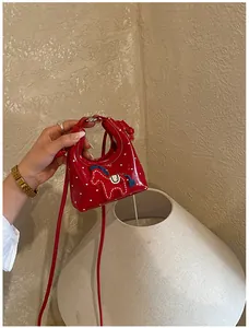 Dettaglio mini borsa in pelle verniciata rossa con pois bianchi e toppa a pony