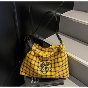 Detail of yellow checkered tote bag featuring black heart embroidery and leather strap