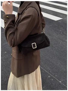 Detail of a dark brown suede crossbody bag with metallic clasp on a stylish street outfit