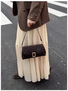 Detail of a dark brown suede crossbody bag with gold buckle on a stylish model