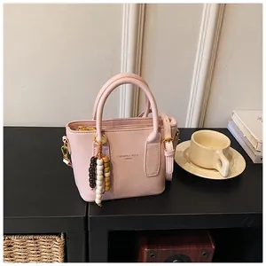 Flache Ansicht einer rosa Leder-Eimertasche mit Perlenanhänger auf einem Schreibtisch