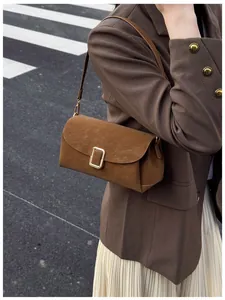 Close-up of brown suede crossbody bag with gold metal buckle on a fashion model
