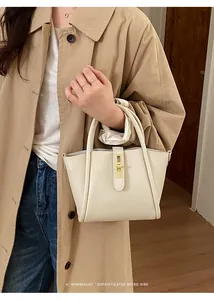Schicke cremefarbene Beuteltasche aus Leder mit goldenem Schloss zu einem stilvollen Trenchcoat