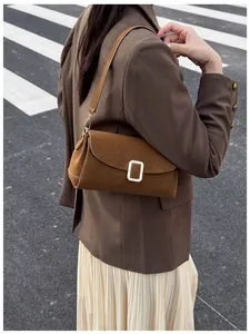 Detail view of a brown suede shoulder bag with a rectangular metal buckle on a model