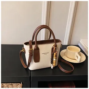 Detailansicht der Retro-Umhängetasche in Creme mit braunem Griff und Perlenanhänger