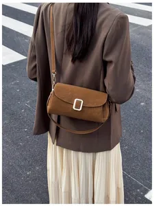 Outdoor street style shot of caramel brown faux suede crossbody bag with silver buckle