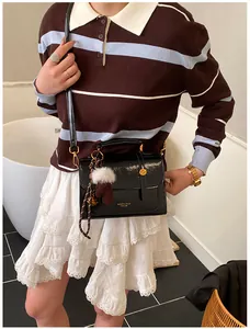 Detail einer schwarzen glänzenden Handtasche mit Goldschnallen und Fellball-Anhänger