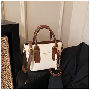 Detail der weißen Umhängetasche mit braunen Griffen und elegantem Perlenanhänger