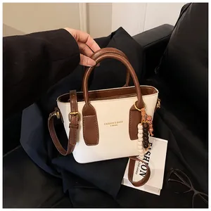 Detailaufnahme der cremefarbenen Retro-Handtasche mit dunkelbraunen Griffen und Goldbeschlägen