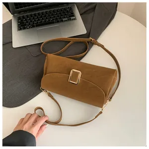 Close-up of caramel brown suede handbag with golden buckle on desk with laptop