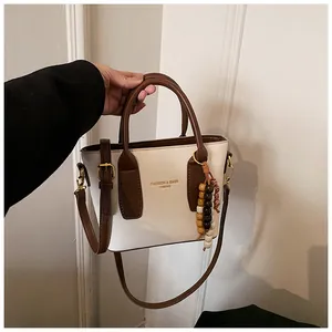 Detail der cremefarbenen Lederbeuteltasche mit bunten Holzperlen und Markenlogo