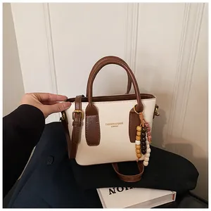 Detail einer minimalistischen Tasche in Creme und Braun mit buntem Perlenanhänger