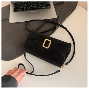 Detail of black suede crossbody bag with gold buckle on a professional office desk