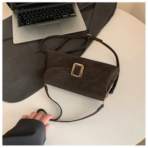 Detailed view of deep brown minimalist crossbody bag with gold buckle on white table