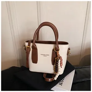 Detail der cremefarbenen Tasche mit braunen Griffen und einem Vintage-Perlenanhänger