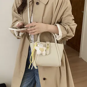 Cremefarbene Beuteltasche mit Akzenten aus Leder und einem süßen Bärenanhänger am Model