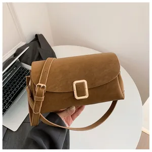 Detail view of brown matte leather shoulder bag with golden metal buckle on office desk
