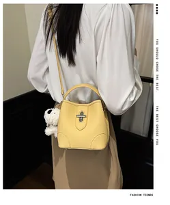 Detail of yellow lychee leather bucket bag with metal twist lock and plush puppy charm