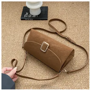 Detail of a brown suede crossbody bag with gold hardware on a textured carpet