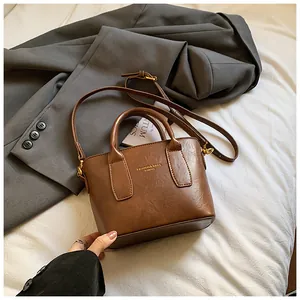 Detail einer braunen Leder-Eimertasche mit goldenen Beschlägen und modischem Text