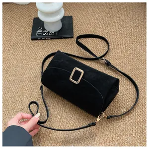 Detail of black suede crossbody bag with gold buckle on a minimalist textured rug