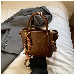 Detail der braunen Vintage-Eimertasche mit Goldschrift und Perlenanhänger-Deko