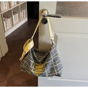 Detailed view of grey plaid tote bag featuring yellow heart embroidery and leather handles