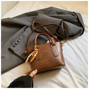 Detail einer braunen Vintage-Handtasche mit goldener Schrift und bunter Holzperlen-Deko