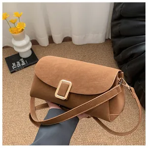 Detail of a brown suede crossbody bag with a large golden metal clasp and slim strap