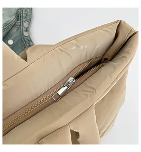Détail de la fermeture éclair en métal argenté sur un sac fourre-tout matelassé beige