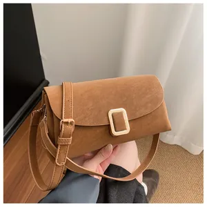 Close-up of brown suede shoulder bag with rectangular gold buckle and adjustable strap