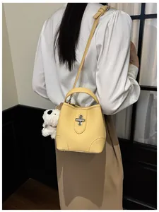 Detail of yellow pebbled leather bucket bag with silver turn-lock and plush puppy charm