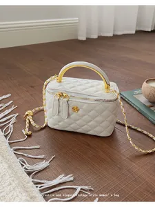 Close-up of white quilted mini box bag with gold floral logo and chain on wooden floor