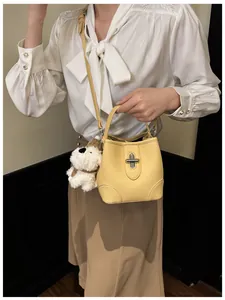 Detail of yellow leather bucket bag featuring a metal lock and plush puppy charm