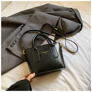 Detail einer schwarzen glänzenden Kunstleder-Eimertasche mit Golddruck auf grauem Anzug