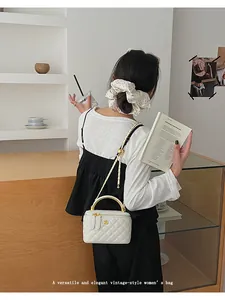 Detail of white quilted mini box bag with gold metal handle and chain shoulder strap