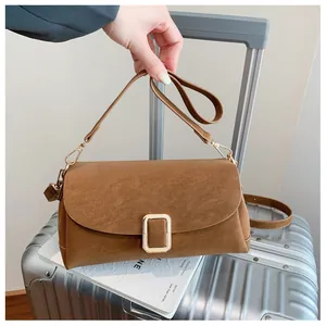 Detail of a brown leather crossbody bag with a large gold rectangular buckle on top of a suitcase