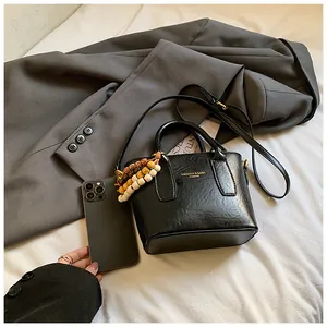 Detailaufnahme der schwarzen Beuteltasche mit Goldlogo und Holzperlenanhänger