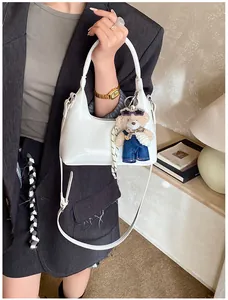 White glossy shoulder bag with cute teddy bear charm shown in a modern lifestyle setting