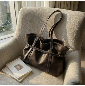 Detail der braunen Vintage-Leder-Tote mit Zierriemen auf einem weich texturierten Sessel