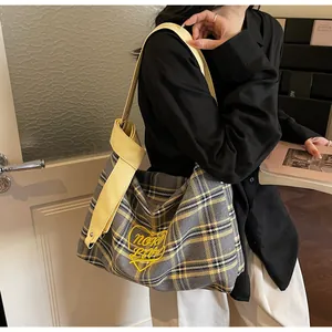 Detail of checkered tote bag featuring yellow heart embroidery and knotted shoulder strap