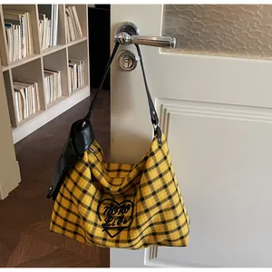 Detail of yellow plaid tote bag featuring heart embroidery and black leather strap
