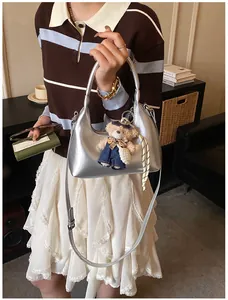 Silver metallic half-moon handbag with teddy bear charm and adjustable shoulder strap