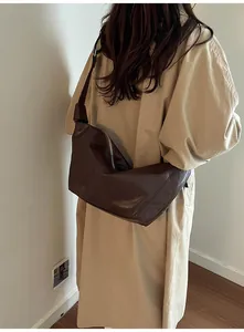 Detailed side view of dark brown leather crossbody dumpling bag on a model wearing a trench coat