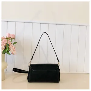 Close-up of black suede envelope crossbody bag with gold hardware and extra strap