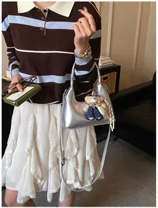 Detail of silver metallic handbag featuring bear charm and plaid scarf accessory