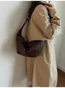 Deep brown semi-moon hobo bag detail with zipper and adjustable strap on a trench coat