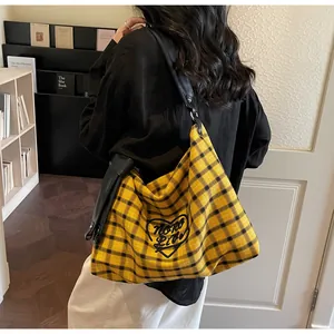 Detail of yellow and black checkered tote bag with embroidered logo and wide leather strap