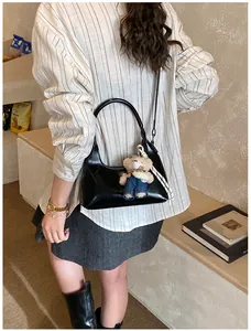 Detail of black glossy crescent bag with a cute teddy bear charm on striped shirt